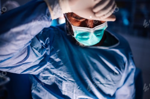 Preview: Surgeon in Blue Scrubs Repositions Mask in a Contemplative Moment