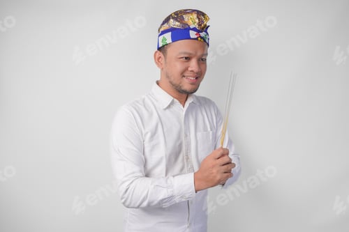 Preview: Balinese man wearing traditional headdress called udeng doing paying respect and holding incense.