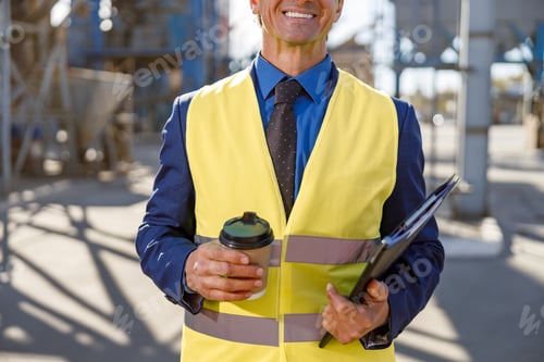 Preview: Cheerful male engineer holding cup of coffee and documents