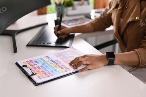 Preview: Cropped shot of creative woman working with color palette and graphic tablet on white table.