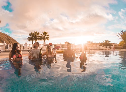 Preview: Happy friends drinking champagne in pool party at sunset