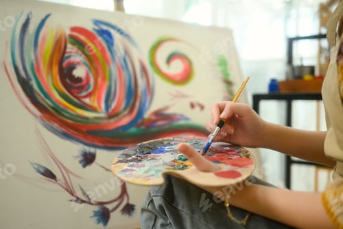 Preview: Close up of female artist mixing paint on a palette while working on her painting in studio