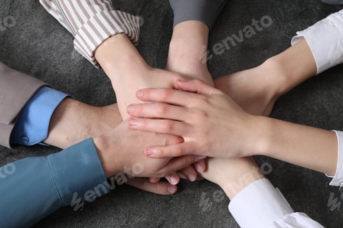 Preview: Business concept. Group of people stacking hands at grey textured table, above view