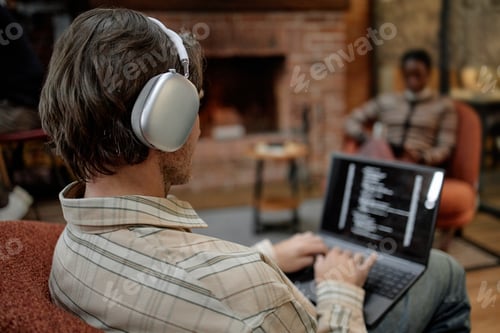 Preview: Young Adult Caucasian Man Using Laptop and Listening to Music in Modern Office