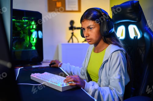Preview: Concentrated young teenage ethnic girl sitting at desk and playing games