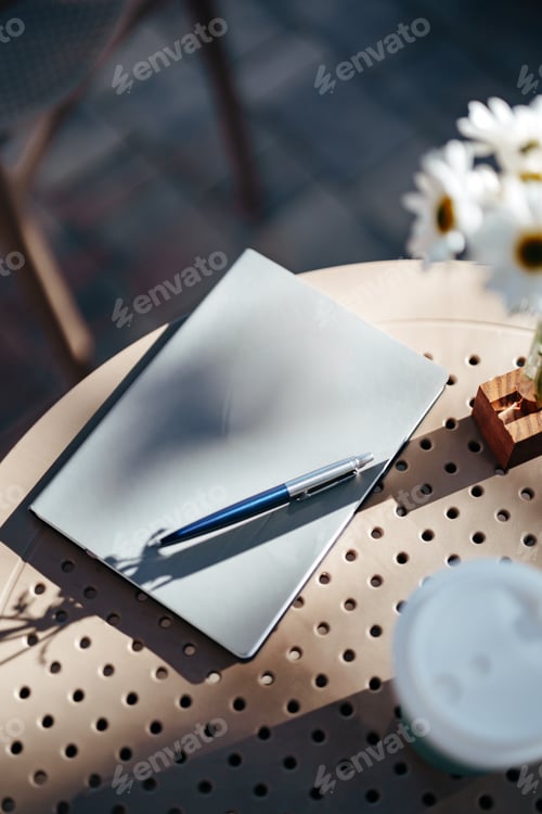 Preview: Notepad and pen on a table in an outdoor cafe with sunny ambiance