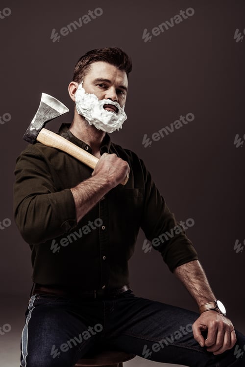 Preview: handsome brave bearded man in brown shirt sitting on chair and holding ax