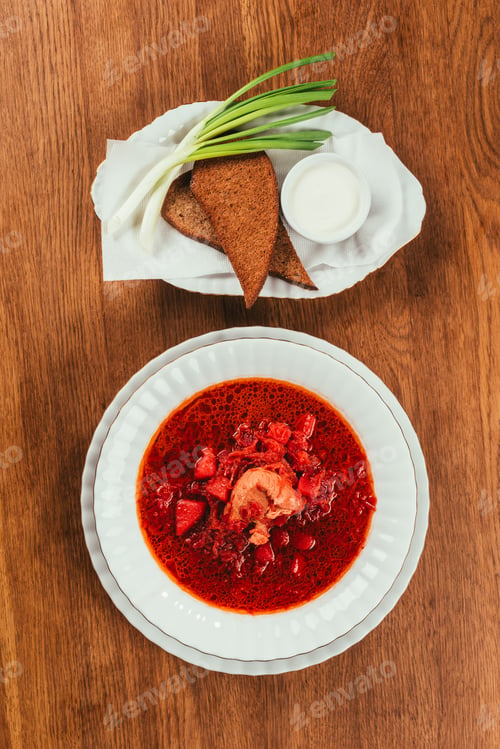 Preview: Top view of borscht dish in white plate served with rye bread on wooden table