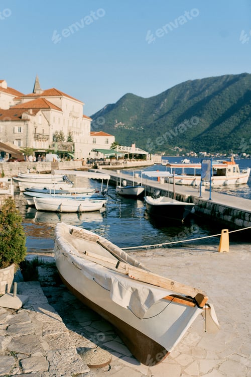 Preview: Fishing boat in a cover lies on the shore near a pier with moored boats. Perast, Montenegro