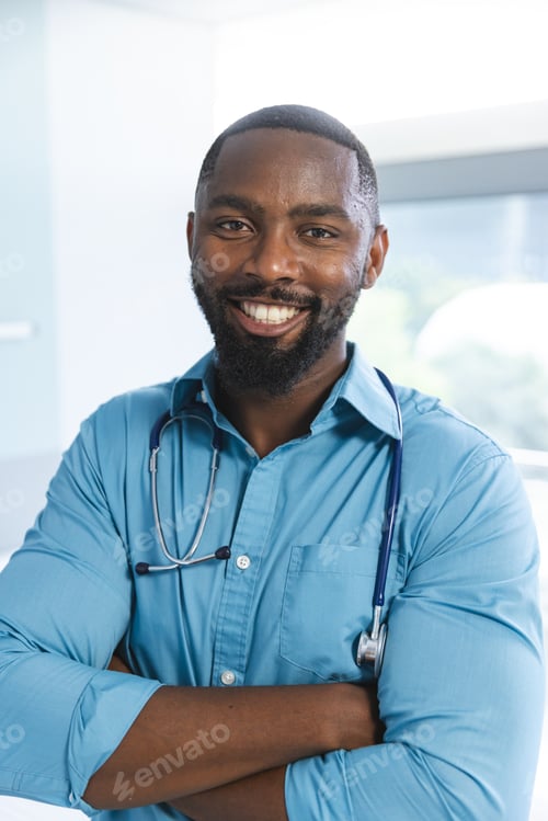 Preview: Portrait of happy african american male doctor wearing blue shirt and stethoscope in hospital room