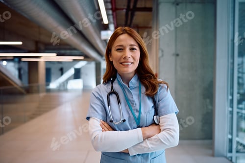 Preview: Portrait of happy nurse with crossed arms at medical clinic looking at camera.
