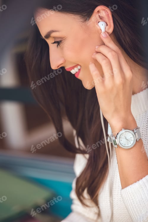 Preview: selective focus of smiling young woman putting on earphones in cafe