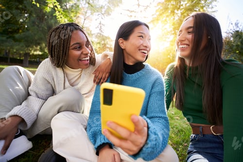 Preview: Three young women using a mobile cell while having fun in the park and laughing. Social media app