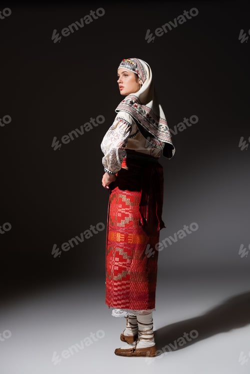 Preview: full length of young ukrainian woman in traditional dress with ornament and headwear posing on black