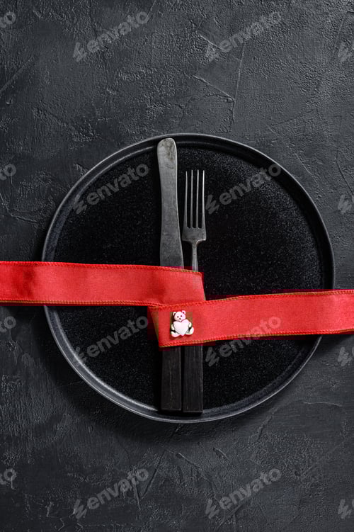 Preview: Valentines day table setting with knife, fork, red ribbon. Black background