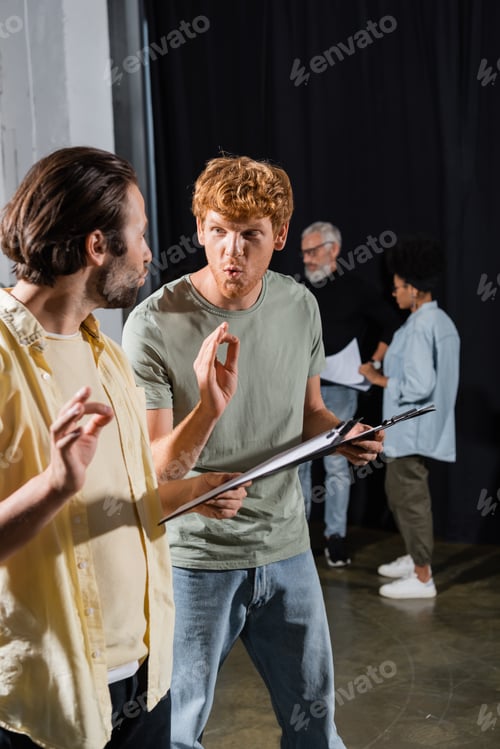 Preview: young actors with clipboards grimacing and showing okay signs during rehearsal in acting school