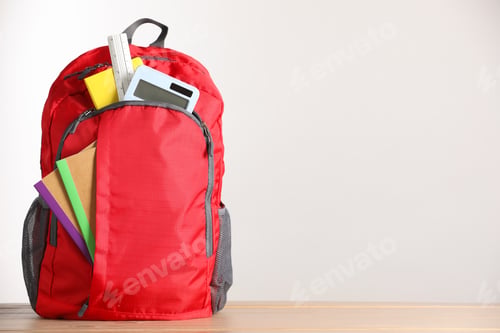 Preview: Red backpack with different stationery on wooden table against light background. Space for text
