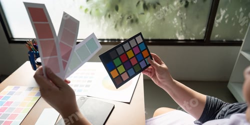 Preview: Graphic designer analyzing color palettes and samples at a creative workspace.