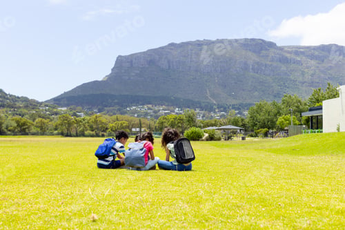 Preview: Three students are sitting on the grass, studying with a mountain in the background