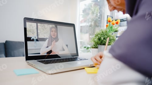 Preview: Asia muslim businesswoman using laptop talk to colleague by video call at living room.