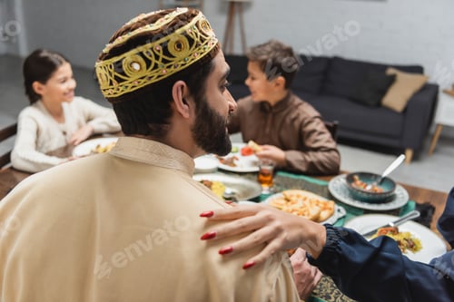 Preview: Muslim woman touching husband near blurred kids during iftar at home