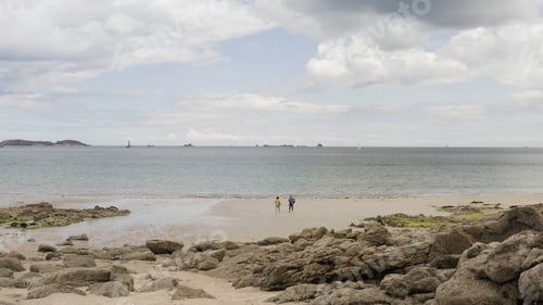Preview: Couple is walking on the beach with stony shore with the calm sea and blue cloudy sky on the