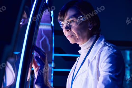 Preview: forward-thinking middle aged woman scientist looking at innovative device in discovery center