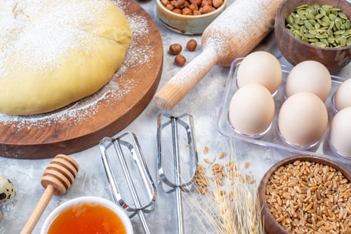 Preview: Side view of raw pastry flour on round board grater fresh fruits eggs honey on gray background