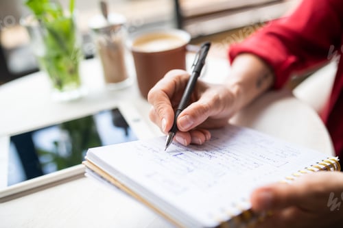 Preview: Hand of young businesswoman with pen making notes on page of notebook