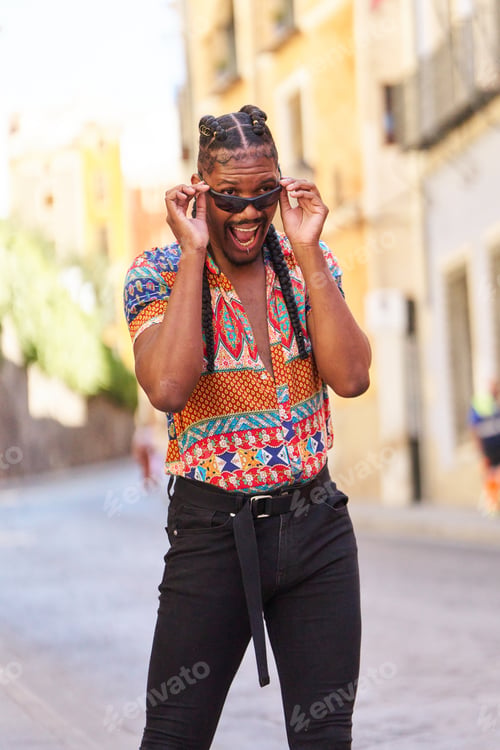 Preview: Stylish gay man wearing heels and adjusting sunglasses in city street