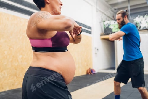 Preview: Pregnant woman and trainer warming up in gym