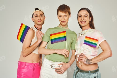 Preview: positive and young lgbt friends with tattoos standing in colorful clothes and holding rainbow flags
