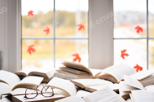 Preview: Multiple open books on a table in front of window with maple leaves with reading glasses