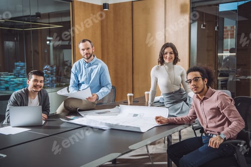 Preview: group of successful architects sitting at conference hall of office and looking at camera