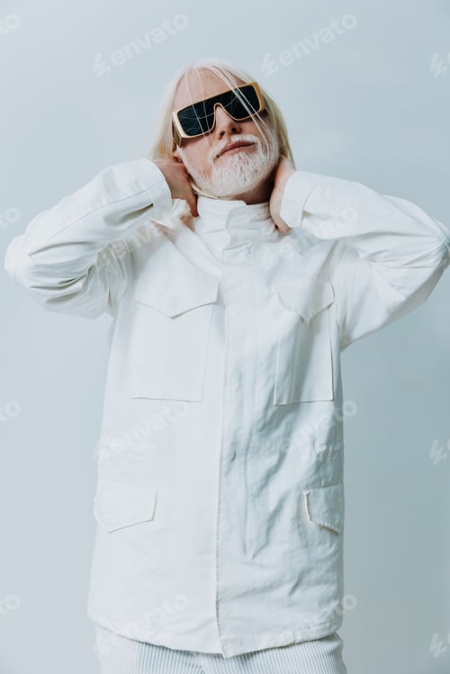 Preview: Fashionable elderly man in white outfit with sunglasses against light background showcasing