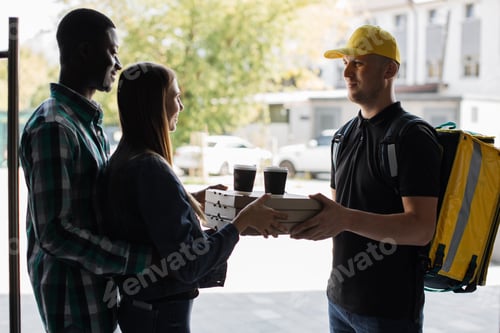 Preview: Male courier giving pizza boxes and takeaway coffee from restaurant to multinational family