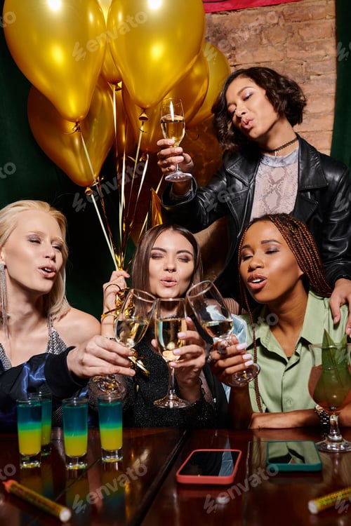 Preview: diverse group of multiethnic girlfriends clinking champagne glasses during birthday party in bar