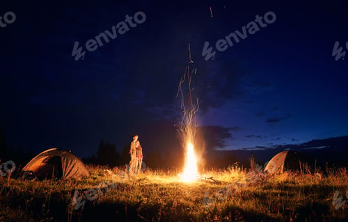 Preview: Young couple standing near campfire under beautiful night sky.