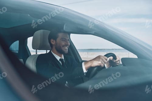 Preview: Feeling the road. Handsome young man in full suit smiling while driving a car