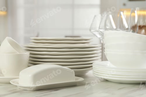 Preview: Clean plates, bowls, cups and glasses on white marble table in kitchen