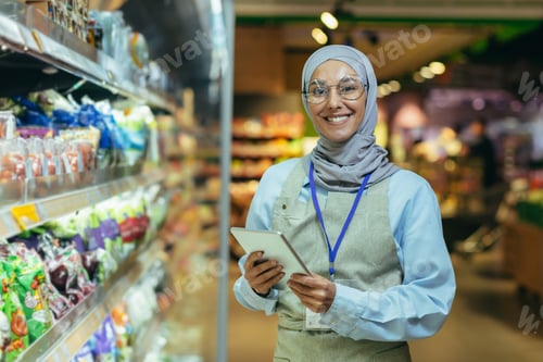 Preview: A young Arab woman in a hijab works in a supermarket, salesperson, manager. Standing with a folder