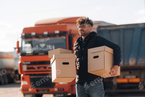 Preview: Boxes in hands. Male worker is near truck outdoors
