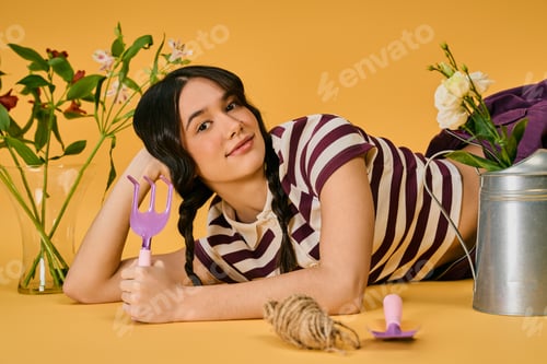 Preview: Joyful young gardener with pigtails delights in plant care in vibrant studio space