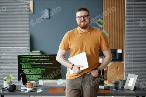 Preview: Portrait of Young Adult Man Smiling While Holding Laptop in Office
