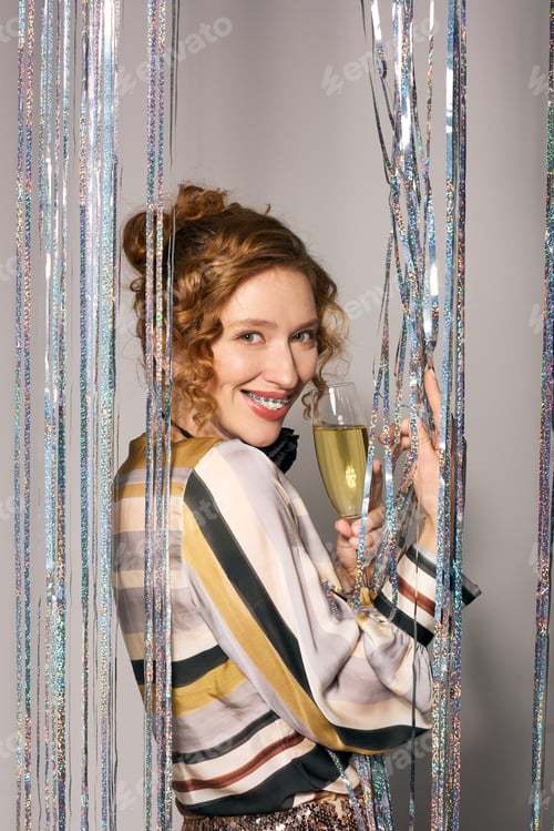 Preview: A cheerful young woman holds a champagne glass, enjoying the moment while wrapping a gift