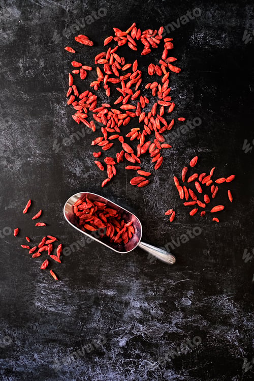 Preview: High angle close up of Goji berries and metal scoop on black background.
