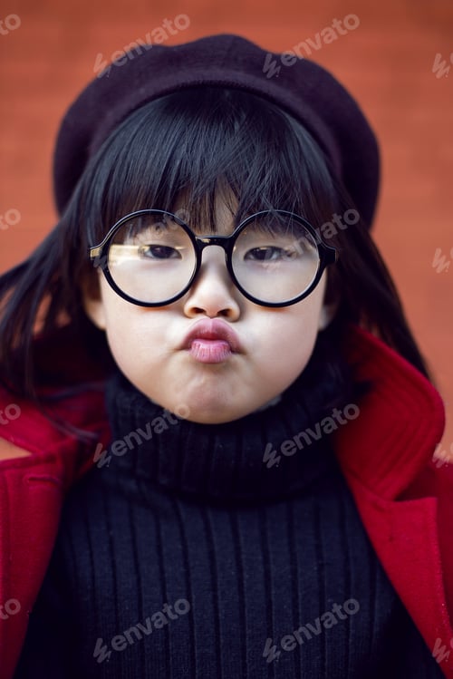 Preview: Korean girl in a red coat and cap and round glasses stands on red brick wall the street in autumn