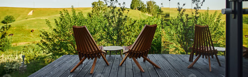 Preview: wooden chairs and coffee table on porch with view on scenic landscape near glass building, banner
