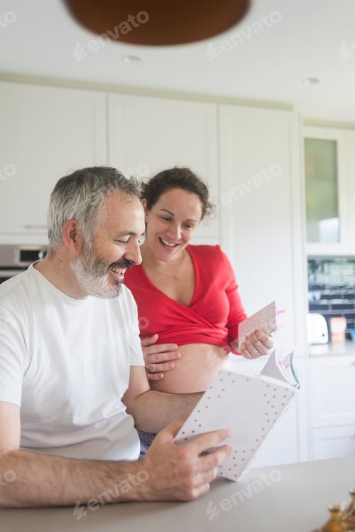 Preview: Smiling Couple Looks at Baby Book in Kitchen