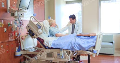 Preview: Male Doctor Wearing White Coat Visiting Senior Female Patient In Hospital Bed Giving Her Good News